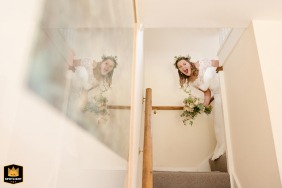 Bride peeking and laughing as she comes down the stairs at her parents’ home in the East Midlands.